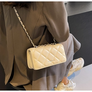 Close-up of beige quilted crossbody bag with metal chain strap worn by a model