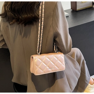 Detail of pink quilted crossbody bag with chain strap worn over a brown blazer
