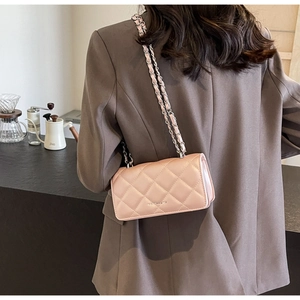 Close-up of pink quilted crossbody bag with chain strap worn by a model in a cafe