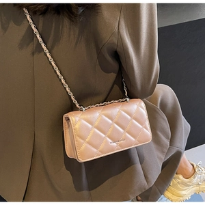 Detail of light pink quilted crossbody bag with metal chain strap on brown blazer