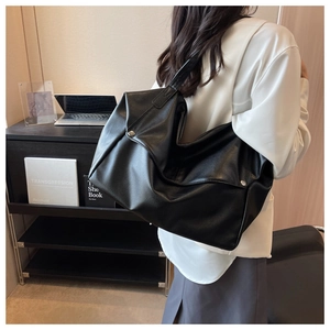 Detail of a large black faux leather tote bag with metallic stud accents and wide shoulder strap