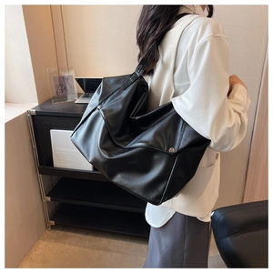 Detail of a large black pebbled leather tote bag with a silver cylindrical metal buckle