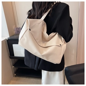 Close-up of a large beige tote bag in lychee pattern faux leather on a model's shoulder