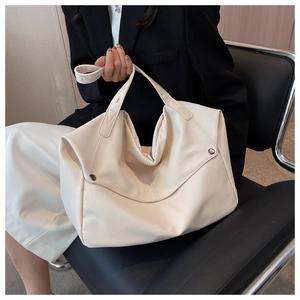Detail of off-white lychee leather tote bag with rivets shown on a seated model