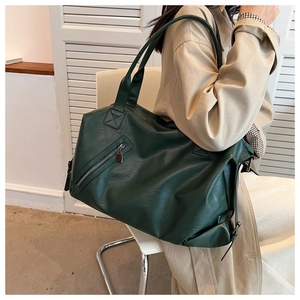 Close-up of a large dark green PU leather tote bag featuring a front zipper pocket detail