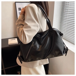 Detail of a large black faux leather tote bag with metal zipper and adjustable side straps