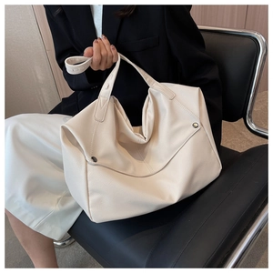 Close-up of beige lychee grain leather tote bag with silver rivets on a leather chair