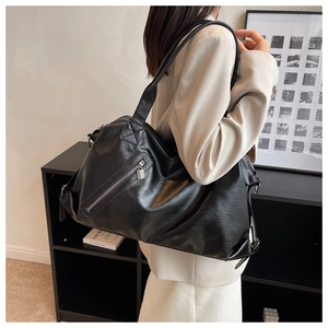 Detail of a large black faux leather tote bag with a side zipper on a female model