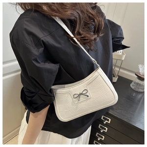 Close-up of white crocodile pattern shoulder bag with a gold bow detail on a model