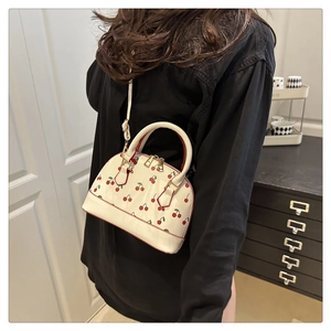 Close-up of white cherry print handbag featuring gold hardware and slim crossbody strap