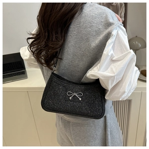 Detail of black sequined shoulder bag with silver metal bow worn by model in a room