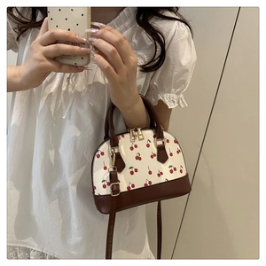 Detail of white cherry print shell bag with brown handles and gold hardware on model