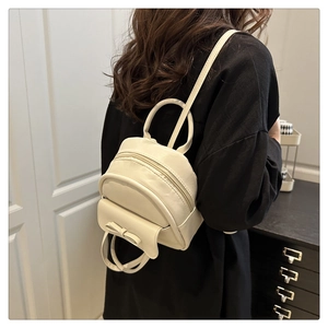 Detail of a creamy white mini backpack with a decorative bow and round top handle