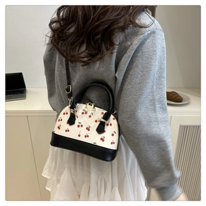Detail of a cherry print shell bag with black handles and adjustable shoulder strap