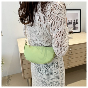 Detail der lindgrünen Leder-Baguette-Tasche mit Goldkette auf einem weißen Spitzenkleid