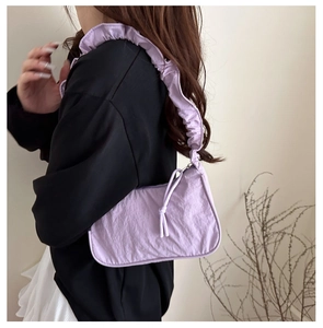 Detail of lavender pleated handbag showing wavy shoulder strap and drawstring knot detail