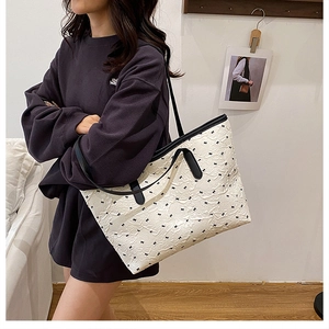 Detail of white embossed tote bag with small black bow prints and long leather handles