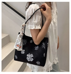 Détail du sac seau noir à fleurs avec un foulard décoratif noué sur l'anse tressée