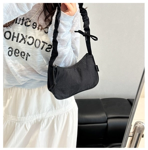 Detail view of black pleated nylon shoulder bag with bow and fashion label on model