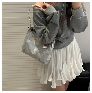 Détail d'un sac cabas en toile avec broderie florale, poignée tissée et foulard en soie