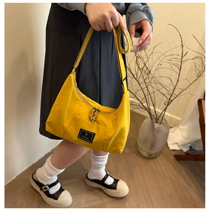 Detailed view of yellow canvas shoulder bag with branded label and zip knot detail