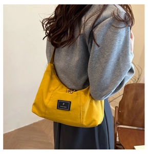 Detail of yellow crescent shoulder bag with branded woven patch on smooth fabric
