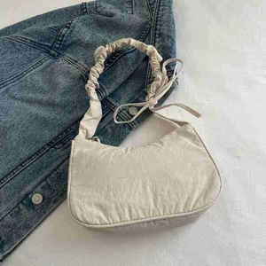 Top view of cream ruched hobo bag with bow shoulder strap detail on denim background