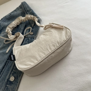 Close-up of beige ruched tote bag with side label on blue denim background