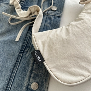 Detail of pleated beige crossbody bag featuring black FANYISSA fabric label on soft texture