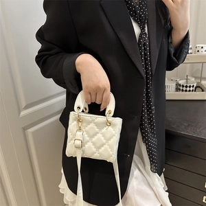 Quilted white mini handbag with golden hardware and adjustable strap shown on a black blazer