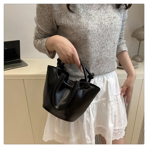 Detail of black glossy bucket bag featuring unique knotted handle and fashion engraving