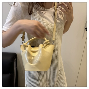 Detail view of pale yellow patent leather bucket bag with drawstring and top handles