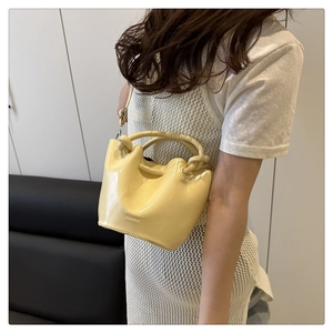 Detail of butter yellow pleated bucket bag with twisted handle and embossed logo text