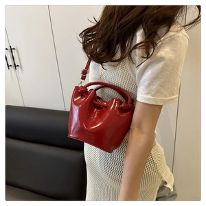 Model wearing red patent leather bucket bag with woven handle and thin shoulder strap