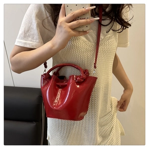 Detail of red patent leather bucket bag with woven handle and detachable shoulder strap