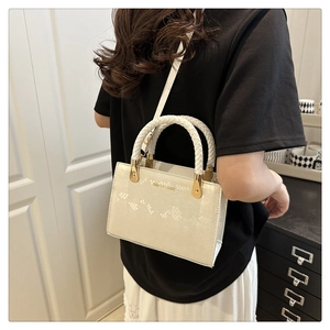 Detailed view of a white crossbody bag featuring a unique woven handle and gold lettering