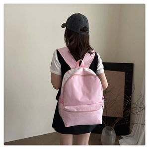 Pink canvas backpack detail with white bold lettering and side mesh storage pocket