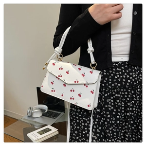 Détail du sac bandoulière blanc à motifs cerises et poignée nouée sur un bureau