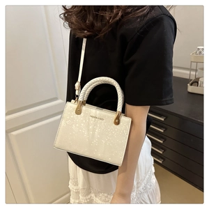 Close-up of beige crossbody bag with woven handle, gold hardware and fashion lettering