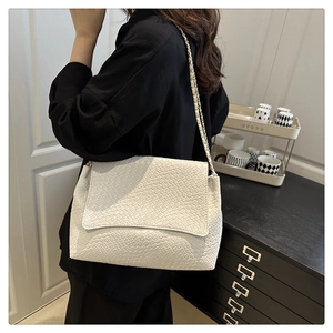 Detail of off-white tote bag featuring woven texture and gold chain shoulder strap