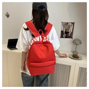 Rear view of a red canvas backpack with white letter printing and side mesh pockets