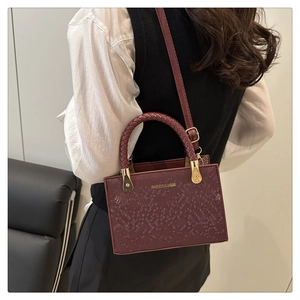 Detail of burgundy stone-pattern tote with woven handle and gold hardware in use