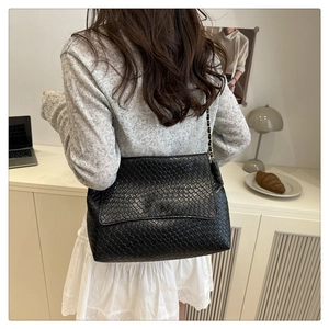 Détail du sac à bandoulière tressé noir avec chaîne en métal sur l'épaule du mannequin