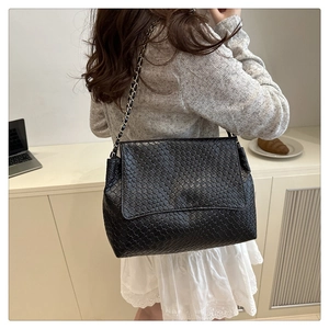 Détail de la texture en cuir tressé et de la bandoulière chaîne d'un sac à main noir élégant