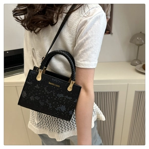 Detail of black faux leather handbag with crocodile pattern and braided top handle