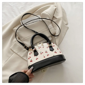 Detail der cremefarbenen Muscheltasche mit Kirschprint, schwarzen Griffen und Golddekor