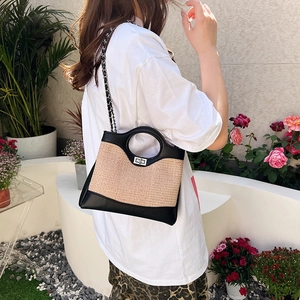 Straw and black leather bucket bag with chain strap shown in a garden setting