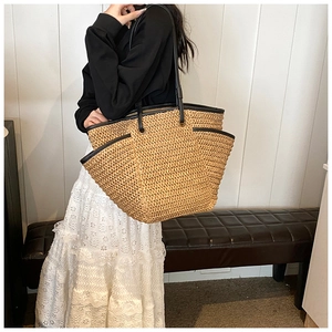 Close-up of woven straw tote bag with black contrast trim and functional side pocket