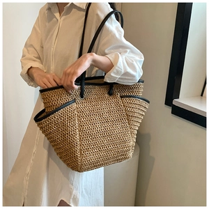 Detail of hand-woven straw tote bag showing black leather piping and long shoulder straps