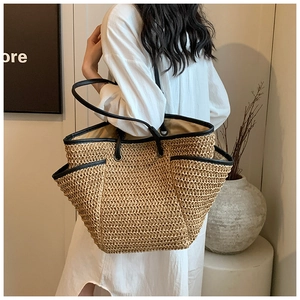Detail of hand-woven straw tote bag featuring black leather straps and reinforced edges